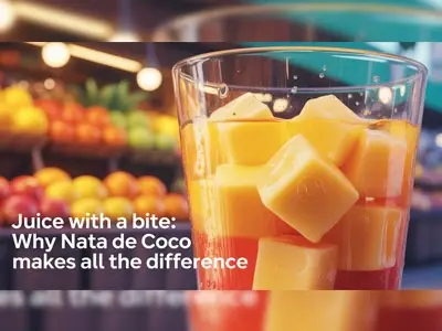 Glass of fruit juice with chunky Nata de Coco cubes in front of a colorful fruit market display.
